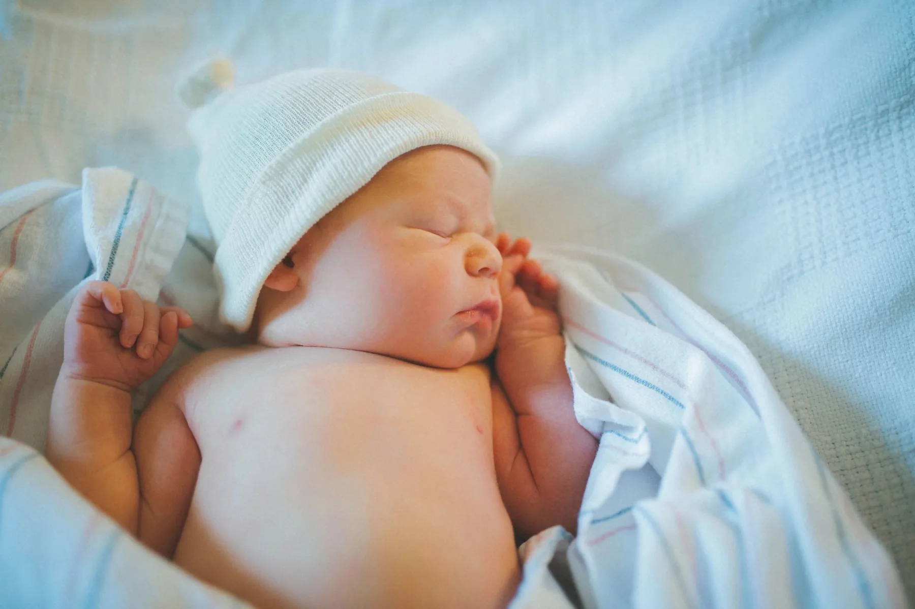 A newborn asleep in a striped hospital receiving blanket, one hand curled up by their face