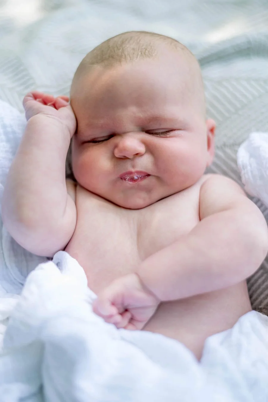 A content, well-fed newborn lying on a blanket with both arms up